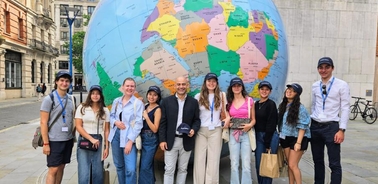 A group of people of various ages standing in front of a large globe map outdoors.