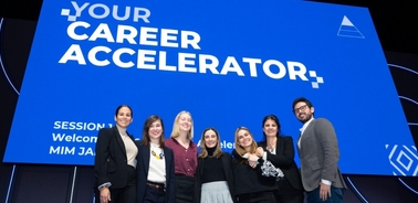 A group of six people smiling in front of a large screen displaying the text 'Your Career Accelerator'.