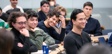 A group of students are smiling and engaging in a classroom setting.