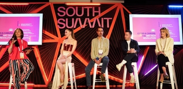 Five people participating in a panel discussion at the South Summit event, sitting on stage in front of a purple and red background with South Summit branding.