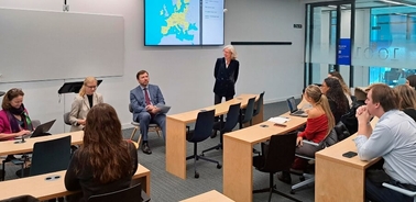 A group of people sitting and listening to a speaker in a modern classroom setting.