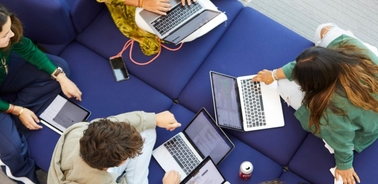 A group of people collaborating on laptops while seated on a couch.