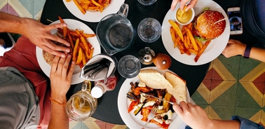 A top view of a table set with burgers, fries, and drinks being enjoyed by several people.