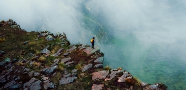 A person standing on the edge of a rocky cliff shrouded in mist.