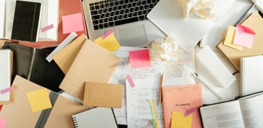 A cluttered workspace filled with books, notebooks, and sticky notes.