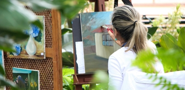 A woman painting in an outdoor setting surrounded by greenery.