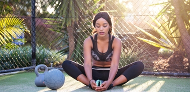 A woman meditating while sitting on the ground in a sunny outdoor gym environment.