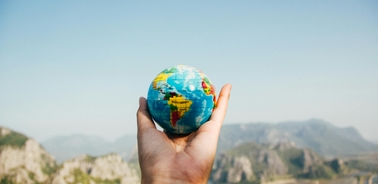 A hand holding a small globe against a scenic mountainous backdrop.