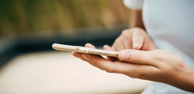 A person holding a smartphone while sitting outdoors.