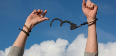 A person breaking free from handcuffs against a blue sky.