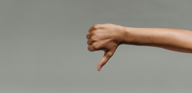 A hand making a thumbs down gesture against a grey background.