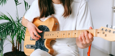 A young woman playing an electric guitar in a bright room with plants.