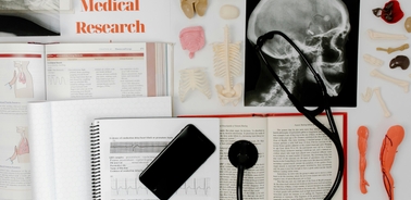 A top-down view of medical research materials including textbooks, anatomical models, a stethoscope, and an X-ray image.