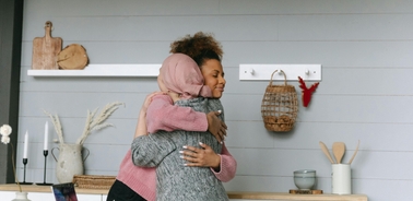 Two women embrace warmly in a cozy indoor setting.