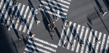 An overhead view of a busy crosswalk with pedestrians and long shadows from the sunlight.