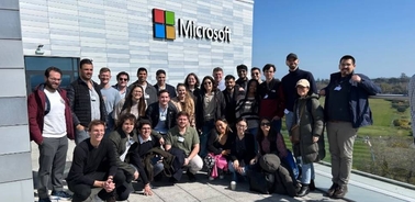 A large group of people posing together in front of a Microsoft building on a sunny day.