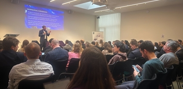 A conference scene with a speaker addressing an audience.