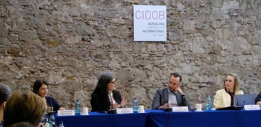 Four people participate in a panel discussion at a conference hosted in a room with stone walls.