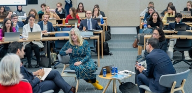 A panel discussion taking place in a modern classroom setting with a diverse group of people engaged in conversation.