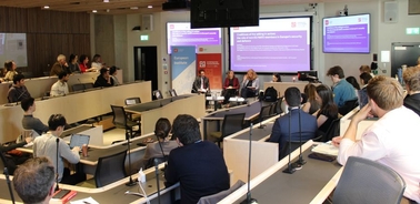 A conference room filled with people attending a panel discussion.