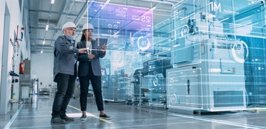 Two professionals are collaborating in a high-tech industrial environment, interacting with digital displays and machinery.