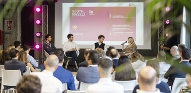 A panel discussion at a conference with four speakers and an audience.