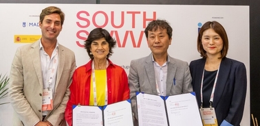 Four people smiling at a conference, standing behind a podium with a South Summit banner and holding documents.