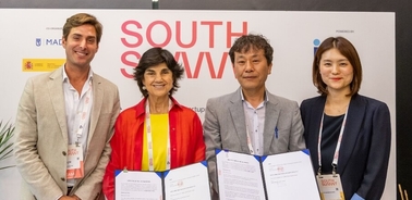 Four individuals standing behind a table at a conference with a 'SOUTH SUMMIT' banner, smiling and holding documents.