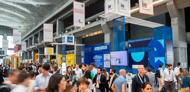 A busy conference hall filled with people and exhibition booths.