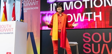 A speaker presenting at the South Summit, dressed in bright orange with a vibrant scarf.