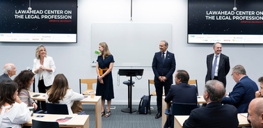 A professional meeting with several individuals engaging in a discussion inside a modern conference room with two large screens displaying 'Lawhead Center on the Legal Profession'.