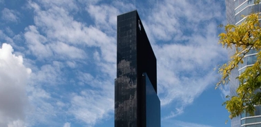 A modern skyscraper with a sleek black facade against a blue sky with white clouds.