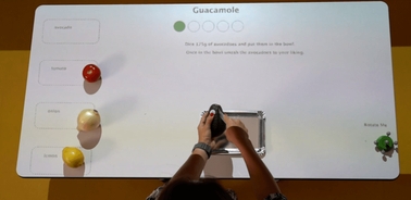 A person is preparing guacamole on a digital interactive table with ingredients displayed.