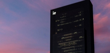 A modern skyscraper with the acronym 'ie' illuminated against a twilight sky.