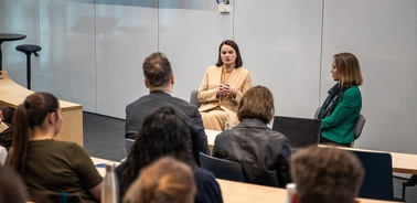 A panel discussion taking place in a modern conference room with two women speakers and an audience.