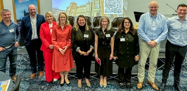 A group of nine people, four men and five women, standing together and smiling at a professional event with name tags.