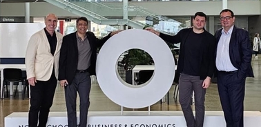 Four men standing around a large circular sign with text at a business event.