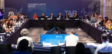 A large conference table filled with participants discussing at the Transatlantic Bridge Conference.
