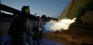 A person is inflating a hot air balloon at dusk using a powerful burner flame.