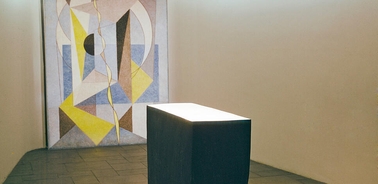 A minimalist interior featuring a geometric mural and a rectangular stone table under soft lighting.