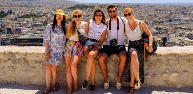 Five people sitting on a stone wall with a panoramic view of a city in the background.