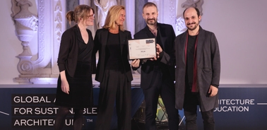 Four people standing on stage, one of them holding an award certificate, at a sustainable architecture event.
