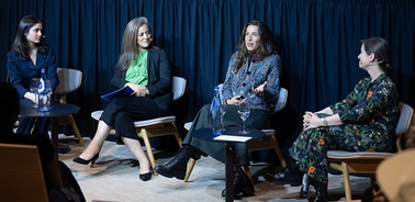 A panel discussion featuring four women seated in a modern setting.