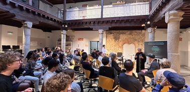 A large group of people attending a presentation in a spacious room with a modern design and historical elements.