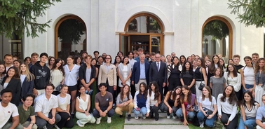 A large group of students and a few adults posing for a photo in front of a white building with arches.