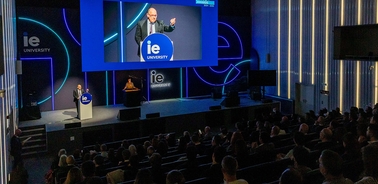 A speaker delivers a presentation at IE University in front of a large audience.