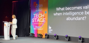 A speaker presents at a women in tech summit, emphasizing the value of intelligence.