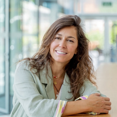 A smiling woman sitting in a modern building environment.