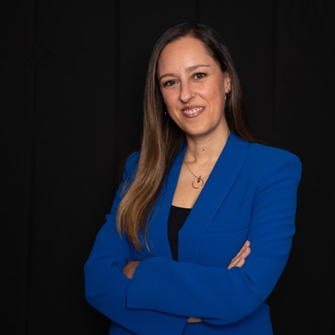A professional woman in a blue blazer stands with crossed arms against a black background.
