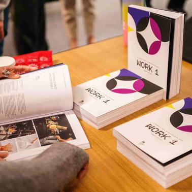 A person is flipping through a book with several copies displayed on a table.